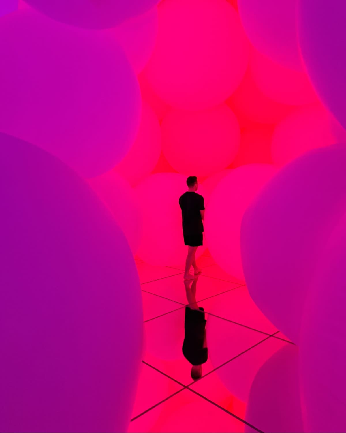 Daniel Klingler von hinten in einer begehbaren Lichtinstallation aus großen, pink leuchtenden Ballons, die sich im Spiegelboden spiegeln